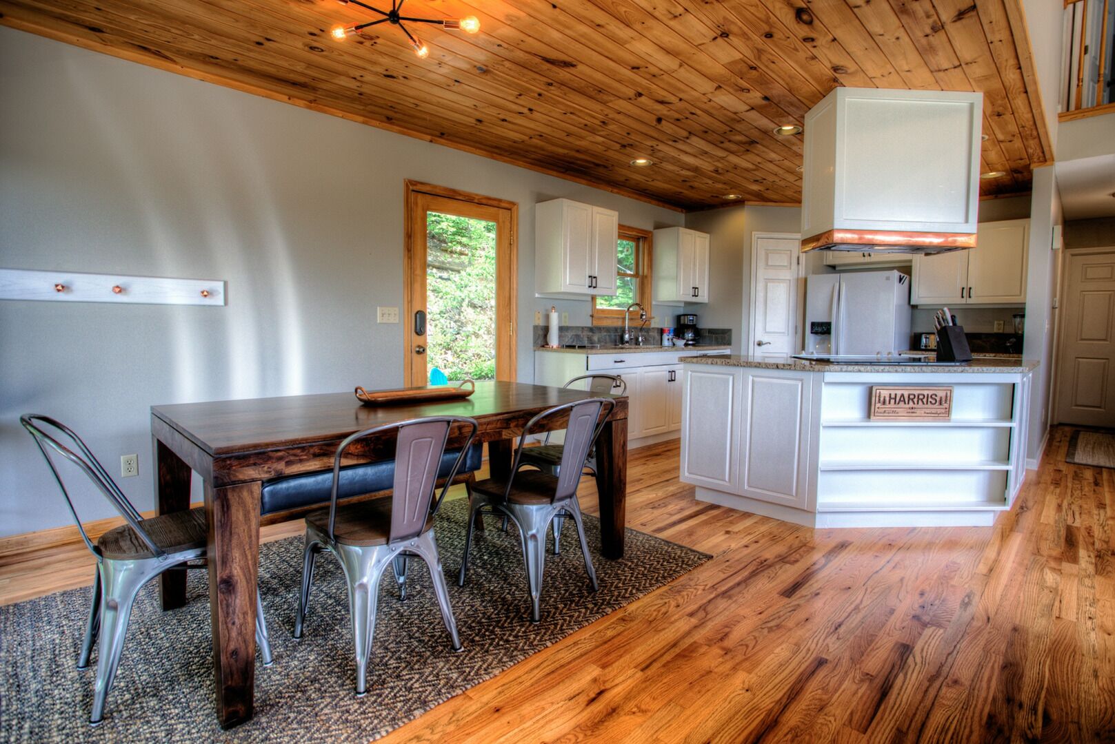 Una cocina moderna con armarios de madera, una isla central y un comedor con mesa de madera y sillas de metal.