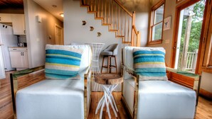 A cozy room with two white leather chairs, a small wooden table, and a staircase leading to an upper level.