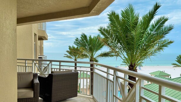 A balcony with wicker furniture, a view of the beach, and palm trees.