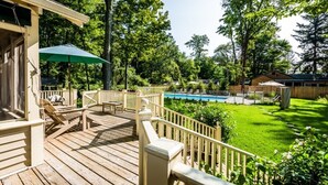 Une terrasse en bois avec des meubles d’extérieur et une piscine en arrière-plan.