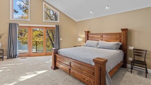 A bedroom with a large bed, a nightstand, a chair, and a view of trees through a sliding glass door. - Hook Lane - Seven Bedroom House, Sleeps 18 (Camdenton)