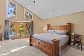 A bedroom with a large bed, a nightstand, a chair, and a view of trees through a sliding glass door. - Hook Lane - Seven Bedroom House, Sleeps 18 (Camdenton)