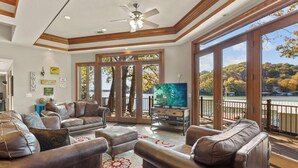 A spacious living room with leather sofas, a flat-screen TV, and large windows overlooking a lake. - Hook Lane - Seven Bedroom House, Sleeps 18 (Camdenton)