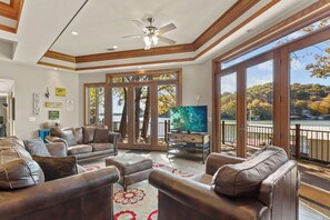 A spacious living room with leather sofas, a flat-screen TV, and large windows overlooking a lake. - Hook Lane - Seven Bedroom House, Sleeps 18 (Camdenton)