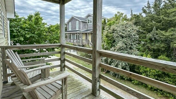 Une terrasse en bois avec une rambarde, un banc et une vue sur une maison et des arbres.