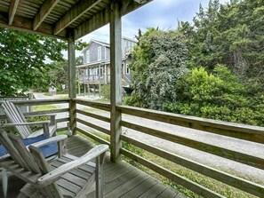 A wooden deck with a railing, a lounge chair, and a view of a house and dense greenery.