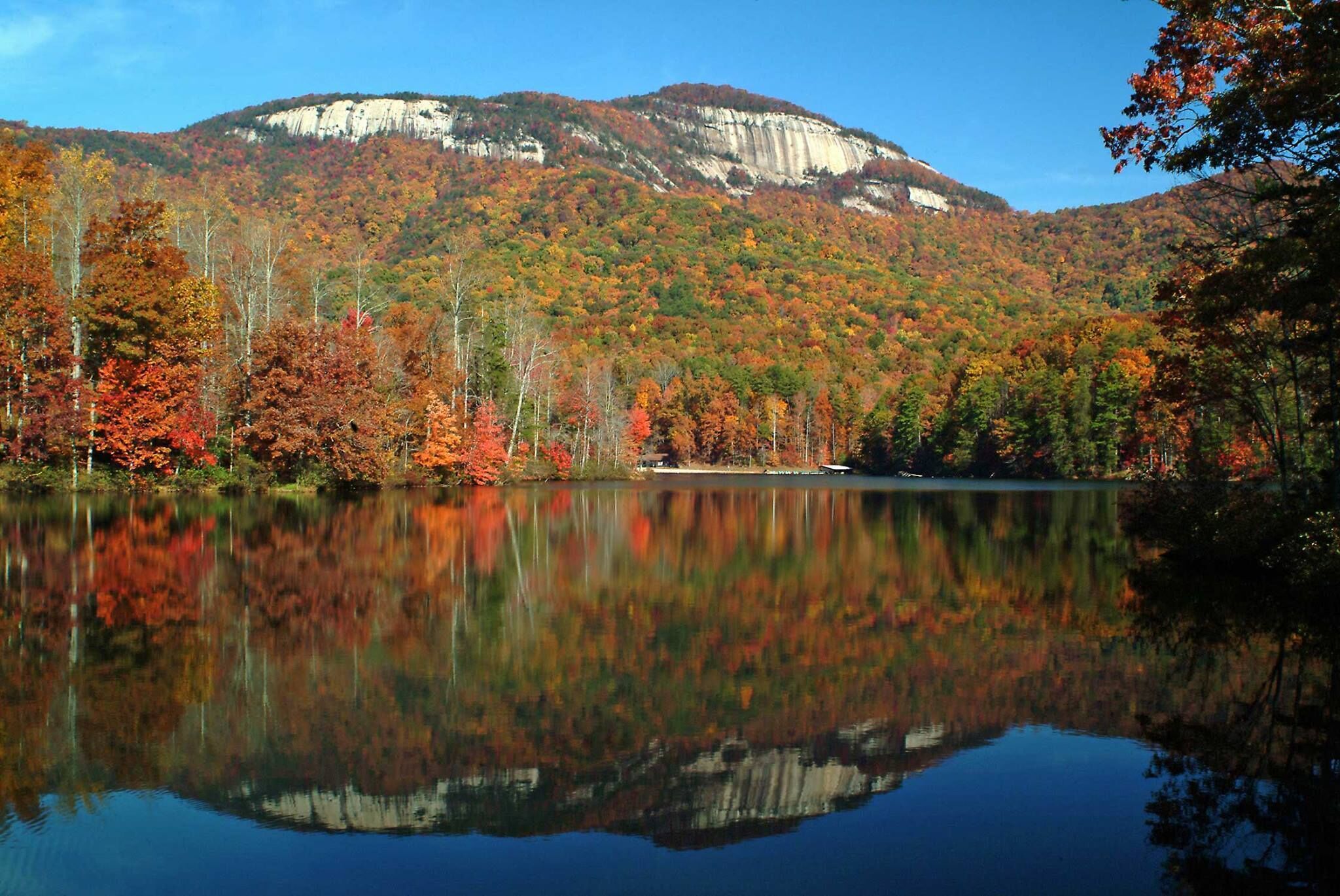 Un lago tranquilo rodeado de follaje otoñal y una montaña al fondo.