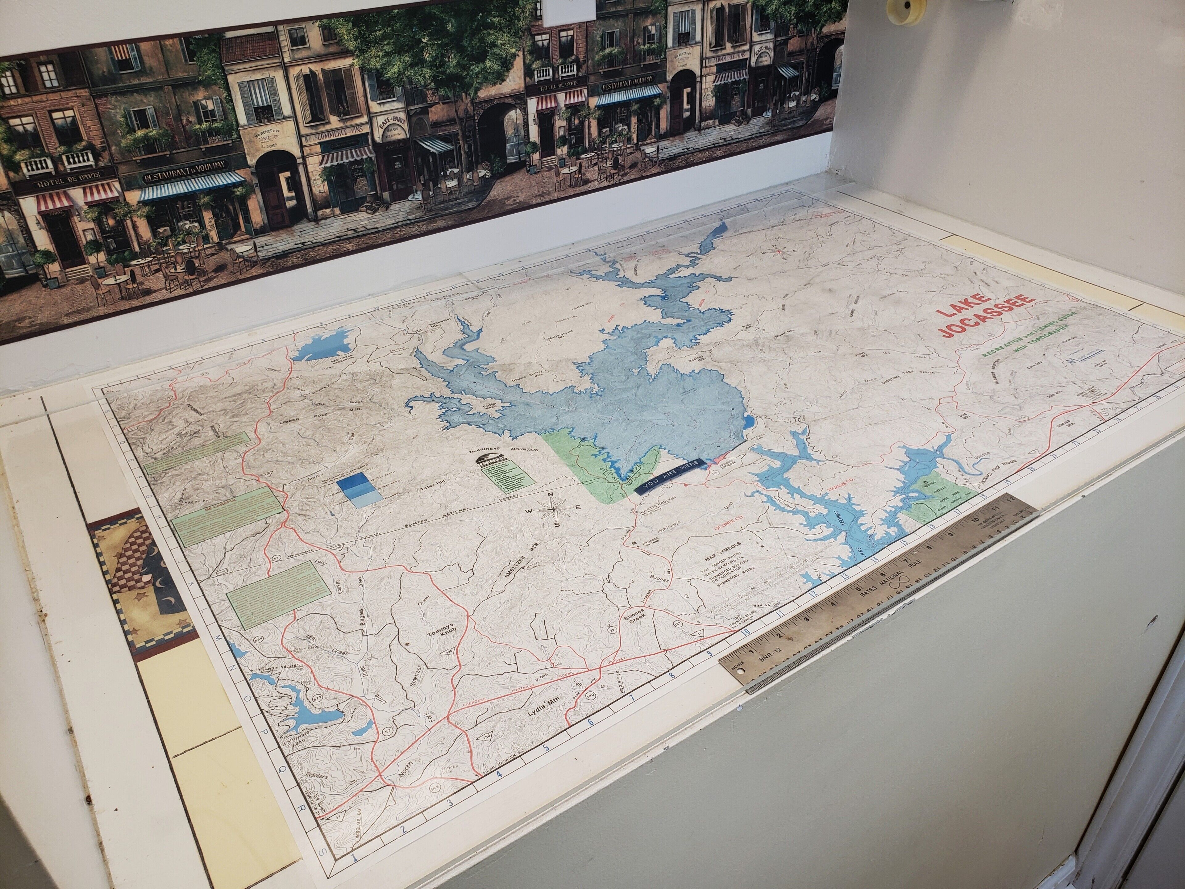 Un mapa detallado con escala, características geográficas destacadas y un pequeño recuadro con una escena callejera.