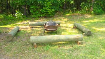 Un terrain de camping avec un foyer entouré de rondins de bois et une zone herbeuse.