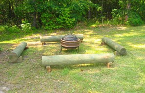 A campsite with a fire pit surrounded by logs and a grassy area.