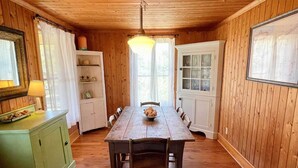 A wooden-paneled room with a dining table, chairs, a chandelier, and a cabinet with a mirror and lamp.