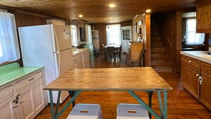 A wooden cabin interior with a kitchen area featuring a wooden table, a refrigerator, and a dining table with chairs.