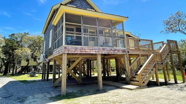 A wooden structure with a balcony and a covered area, supported by wooden stilts.