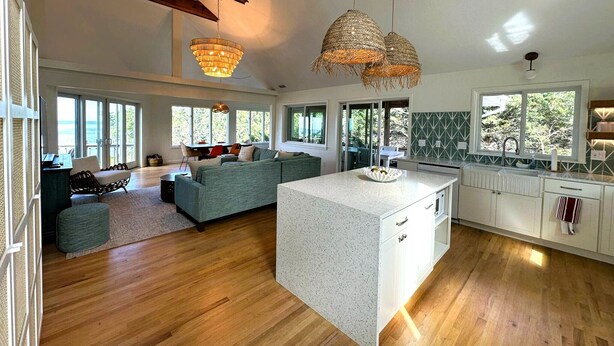 Amplia sala de estar con una isla grande, piso de madera y vistas al exterior.