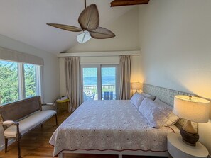 A bedroom with a bed, a bench, a table, a lamp, and a ceiling fan.