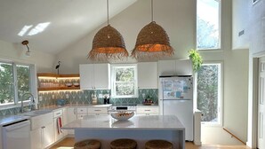 Una cocina moderna con una isla central, armarios blancos y un ventanal que proporciona luz natural.