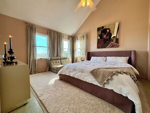 A bedroom with a large bed, a chair, a bedside table, and a painting on the wall.