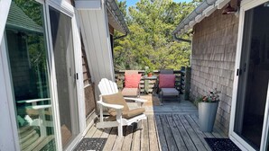 Um deck de madeira com móveis de exterior, incluindo cadeiras e uma mesa, e uma porta de correr de vidro.