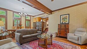 A spacious living room with a large glass coffee table, a beige sofa, a white armchair, and a patterned rug.