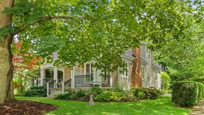 A two-story house with a porch, a brick chimney, and a well-maintained lawn.