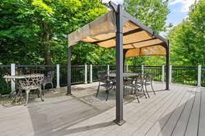 Une terrasse extérieure dotée d’une pergola offrant de l’ombre, entourée d’une terrasse en bois et d’une clôture en métal.