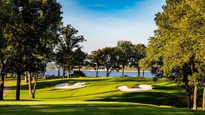 A golf course with sand bunkers, trees, and a body of water in the background. - Get Busy Livin! Grand Lake Waterfront (Afton)