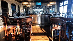 A bar area with wooden chairs and tables, a bar counter with bottles, and a stone wall. - Get Busy Livin! Grand Lake Waterfront (Afton)