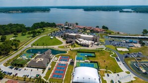 An aerial view of a resort with multiple tennis courts, a large building, and a body of water in the background. - Get Busy Livin! Grand Lake Waterfront (Afton)