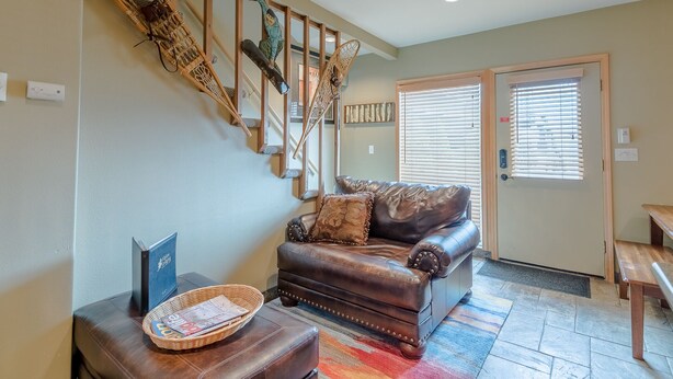 A living room with a brown leather sofa, a wooden staircase, and a wicker chair. - Alpine Villa Condo 24 - Snug as a Bug in this Homey Remodeled Pad (Ketchum)
