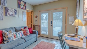 A living room with a grey sofa, colorful cushions, a wooden coffee table, and a door leading outside. - Alpine Villa Condo 24 - Snug as a Bug in this Homey Remodeled Pad (Ketchum)