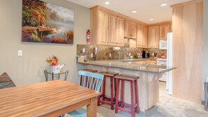 A modern kitchen with wooden cabinets, a granite countertop, and a bar area with stools. - Alpine Villa Condo 24 - Snug as a Bug in this Homey Remodeled Pad (Ketchum)