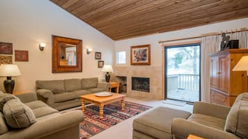 A cozy living room with a fireplace, wooden ceiling, and a view of the outdoors.