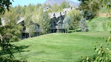 A large, multi-story building with a prominent balcony, surrounded by lush greenery and a mountain in the background.