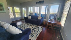 A living room with a dark blue sofa, a patterned rug, and a view of the ocean through large windows. - Daydreamer:  Reverse floorplan home offering three master bedrooms. (Ocracoke)