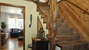 A wooden staircase with stone steps leading to a second floor. A wooden chair and a small table with a lantern are placed near the staircase. - Better Days: Pet friendly home with enclosed yard. Screened porch. (Ocracoke)
