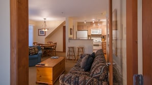 A living room with a sofa, coffee table, and a dining area with chairs and a table. A kitchen with cabinets and appliances is visible in the background. - Convenient Village Location, Free Parking & WiFi, Jet Tub, Ground Floor (Whistler)