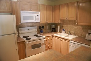Una cocina con armarios de madera, una estufa blanca, un microondas, una cafetera y un fregadero.