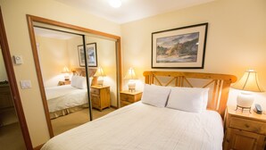 A hotel room with a large bed, two bedside tables with lamps, a wooden headboard, a mirror, and a framed picture on the wall. - Convenient Village Location, Free Parking & WiFi, Jet Tub, Ground Floor (Whistler)