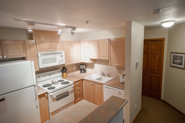A compact kitchen with wooden cabinets, a microwave, stove, and a dishwasher.