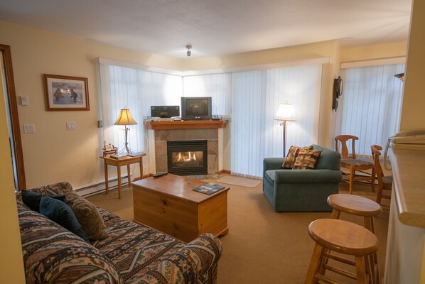 A living room with a fireplace, a television, a sofa, a coffee table, and a dining area with a chair. - Stoney Creek Lagoons 5 (Whistler)