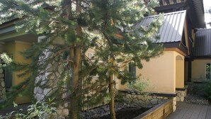 A building with a stone wall, a wooden bench, and a small garden area with plants and a tree. - Convenient Village Location, Free Parking & WiFi, Jet Tub, Ground Floor (Whistler)