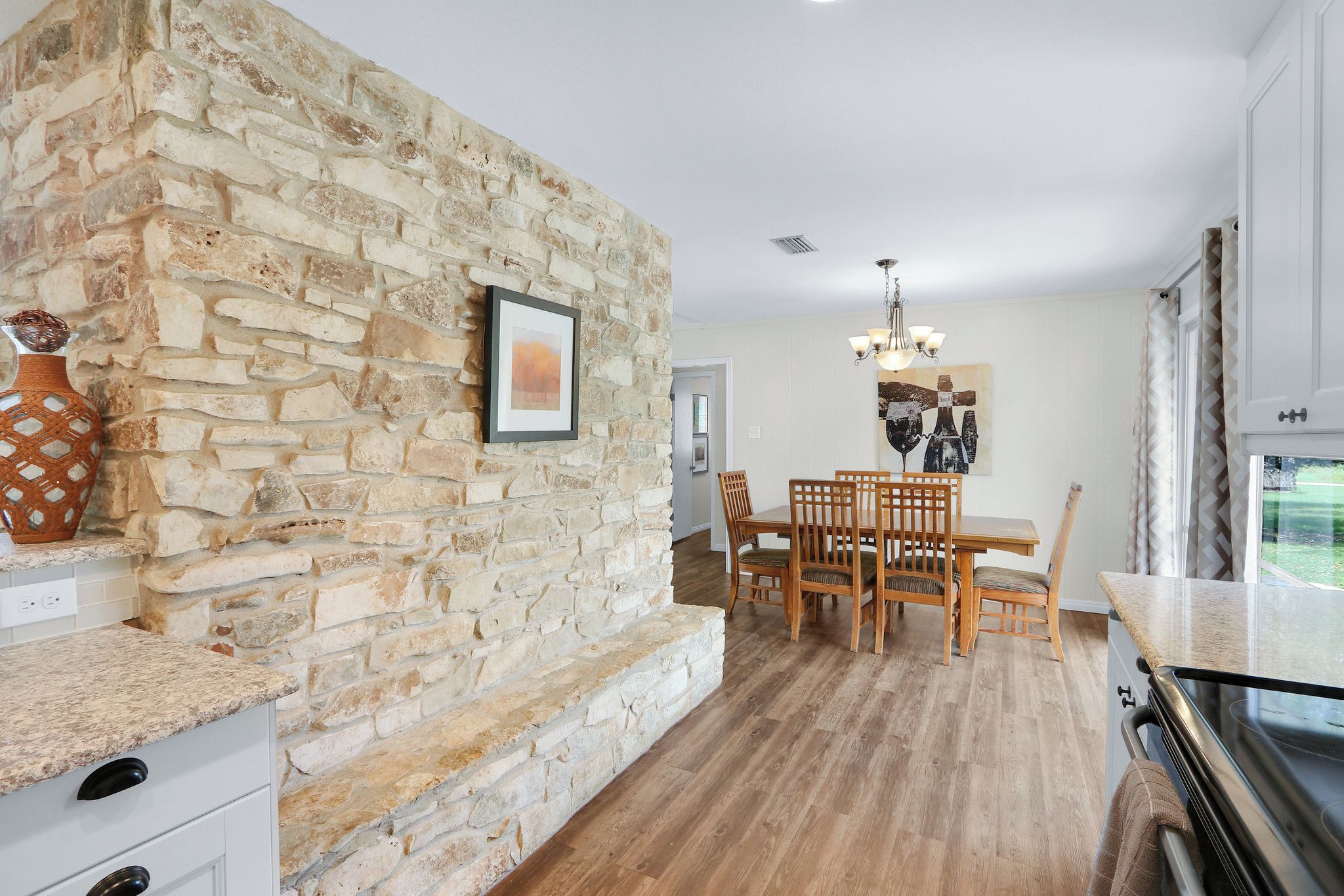 A kitchen with a stone wall, wooden dining table, chairs, and a chandelier.