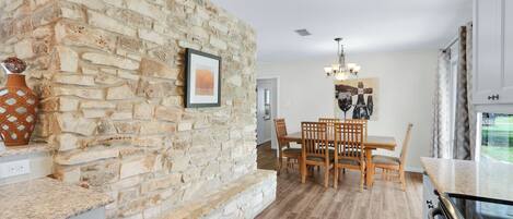 A kitchen with a stone wall, wooden dining table, chairs, and a chandelier.