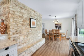 Une cuisine avec un mur en pierre, une table à manger en bois, des chaises et un lustre.