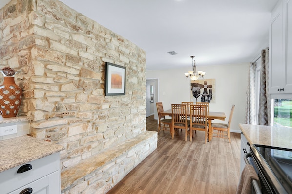 Una cocina con pared de piedra, mesa de comedor de madera, sillas y una araña.