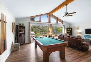 Une table de billard dans une pièce dotée d’un haut plafond et de grandes fenêtres, ainsi que d’un canapé et d’un téléviseur.