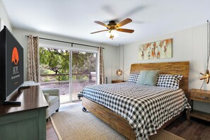 Une chambre avec un grand lit, un ventilateur de plafond, une vue sur l’extérieur et un tableau au mur.