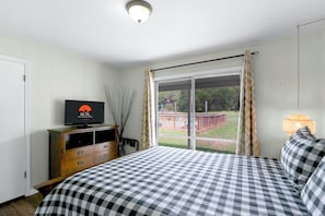 Habitación de hotel con una cama, televisor, cómoda y ventana con cortinas.