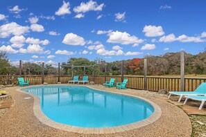 Une piscine entourée d’une terrasse en bois et d’une clôture en bois, avec plusieurs chaises longues turquoise.