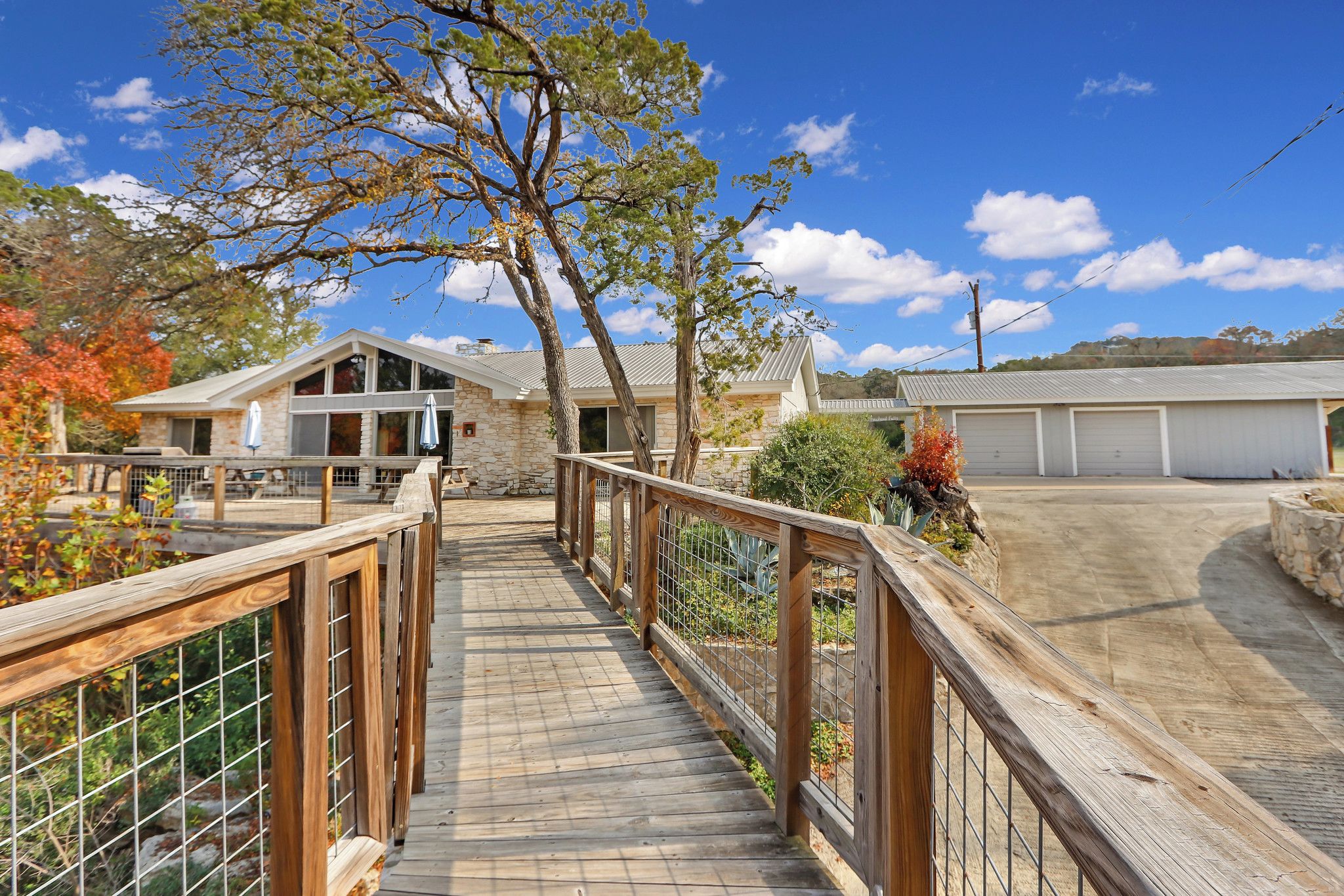 A wooden deck leading to a stone building with a garage in the background.